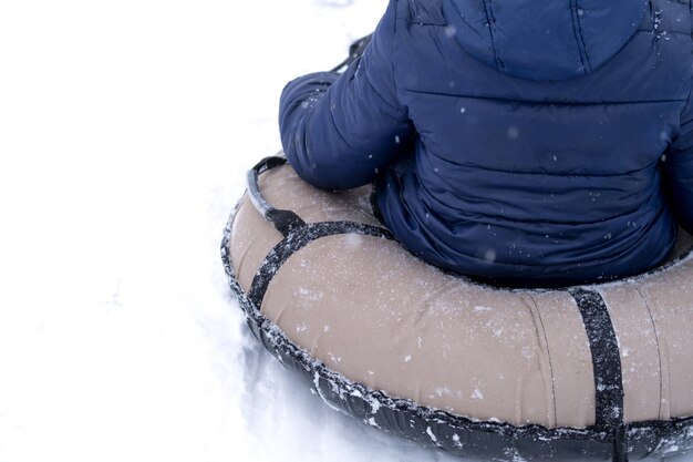 Un ragazzino carino con una tuta scura scivola giù da uno scivolo di ghiaccio, giochi per bambini in inverno, un bambino nel parco in inverno. Ragazzino che si diverte estremo in inverno sui tubi