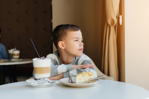 Un ragazzino carino è seduto in un caffè e guardando una torta e il primo piano di cacao. Dieta e corretta alimentazione.