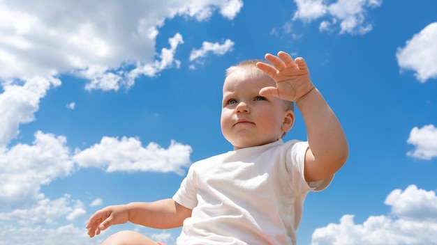 Un ragazzino carino è seduto in una giornata di sole guardando in lontananza Bambino felice sullo sfondo del cielo estivo blu con nuvole Concetto di immaginazione di sogno d'infanzia