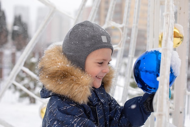 Un ragazzino carino guarda nella palla di Natale e sorride in inverno nel parco