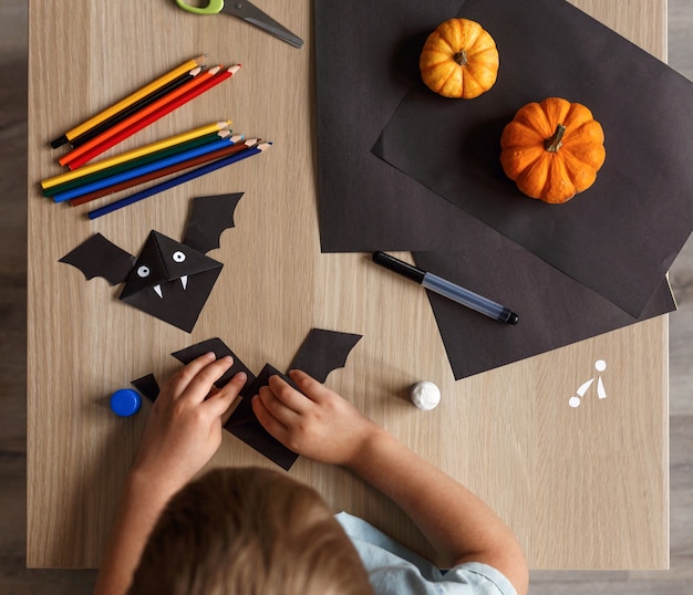 Un ragazzino carino ha realizzato un pipistrello di Halloween con carta nera. Lavoro manuale dei bambini.