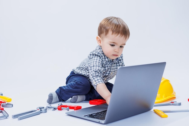 Un ragazzino carino in una camicia a scacchi si siede su uno sfondo bianco con un computer portatile Giocattoli per bambini