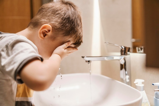 Un ragazzino carino si sta lavando la faccia in bagno