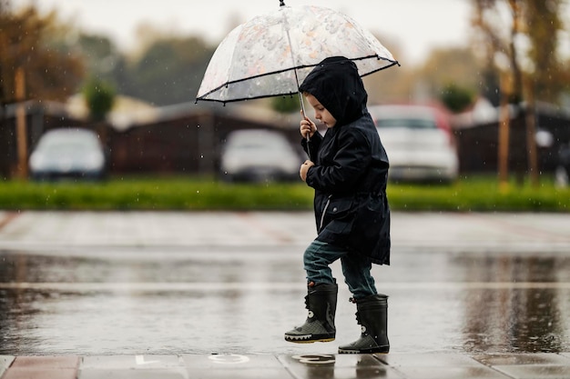 Un ragazzino carino sta camminando per strada con il suo ombrello in un tempo piovoso