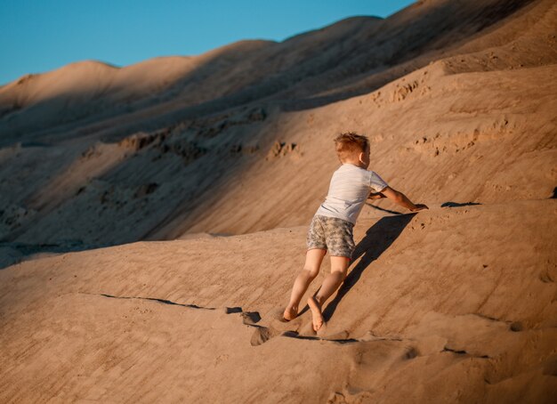 Un ragazzino carino su una montagna di sabbia e gioca. Su una montagna di sabbia in estate.
