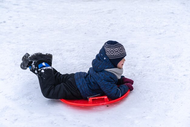 Un ragazzino cavalca una slitta da uno scivolo invernale. Vacanze invernali.