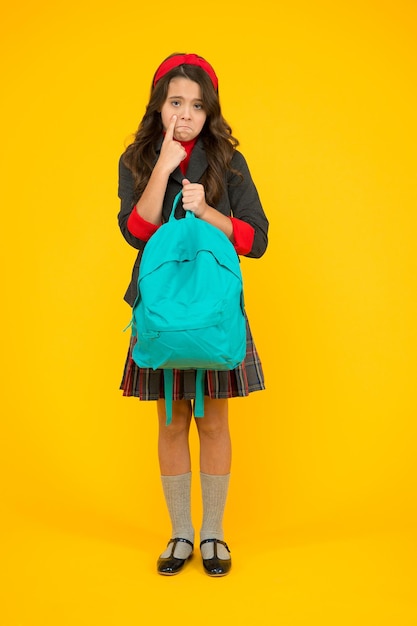 Un ragazzino che piange infelice tiene la borsa della scuola indossando l'uniforme formale sfondo giallo, torna a scuola.