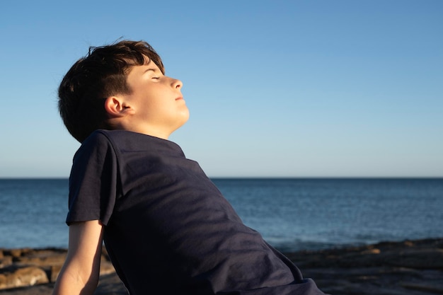 Un ragazzino che si diverte sulla costa a respirare l'aria fresca del mare con gli occhi chiusi.