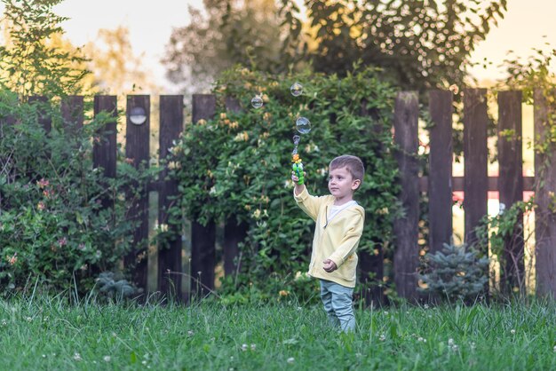 Un ragazzino che soffia bolle di sapone nel giardino estivo