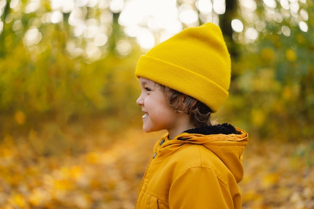 Un ragazzino con un cappello giallo e una giacca cammina attraverso la foresta autunnale, il bambino è attivo nella natura