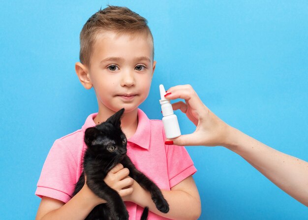 Un ragazzino con un gattino in braccio e la mano di sua madre con spray nasale antiallergico sul blu