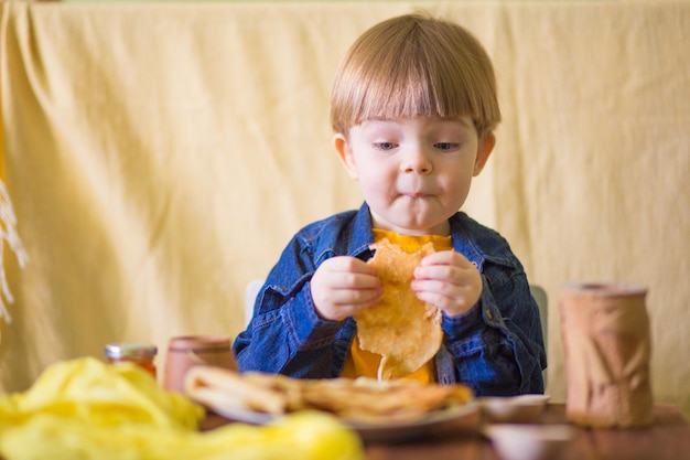 un ragazzino con un sorriso mangia deliziose frittelle con marmellata