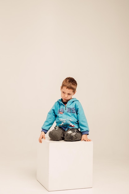 Un ragazzino con una camicetta blu si siede su un cubo bianco in una stanza luminosa