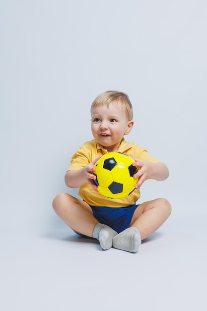 Un ragazzino con una maglietta gialla con un pallone da calcio in mano sorride isolato su uno sfondo bianco Bambino sportivo che tiene una palla Gioco sportivo per bambini Piccolo atleta