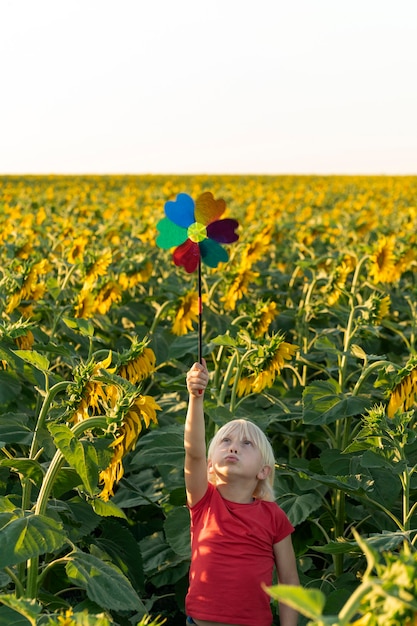 Un ragazzino dai capelli biondi è in piedi tra un campo di girasoli e un mulino a vento sollevato in alto sopra la sua testa.
