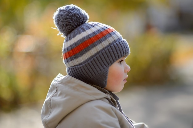 Un ragazzino di 3 anni con un cappello in primo piano sullo sfondo di un parco autunnale
