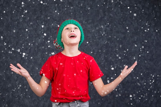 Un ragazzino divertente con una maglietta rossa cattura la neve volante.