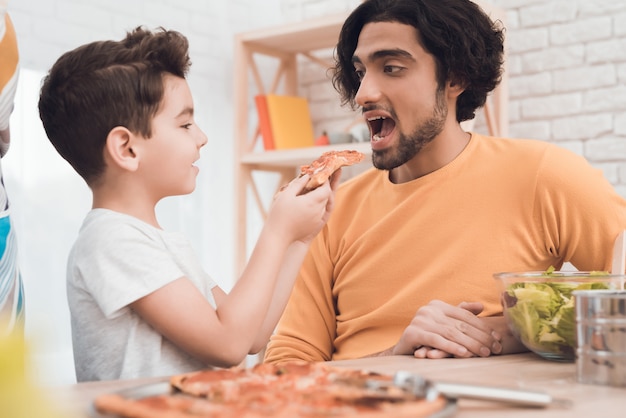 Un ragazzino e suo padre arabo mangiano insieme la pizza.