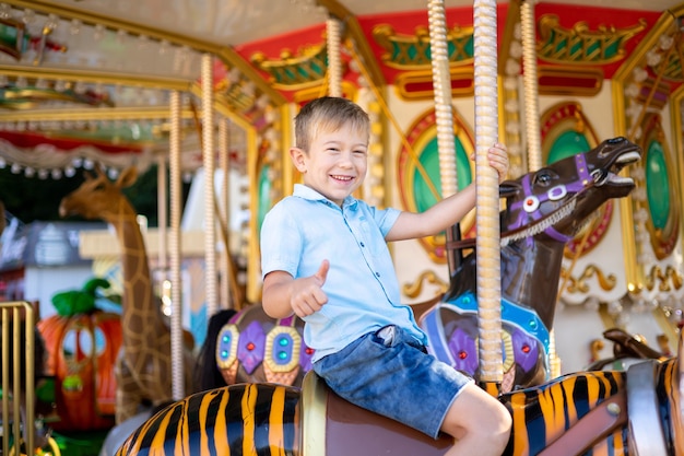 Un ragazzino è un bambino biondo in un parco di divertimenti, a cavallo di una giostra, sorridente, gioioso