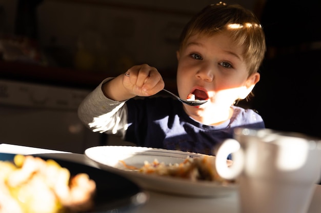 Un ragazzino fa colazione al tavolo mangia con un cucchiaio e guarda nella telecamera