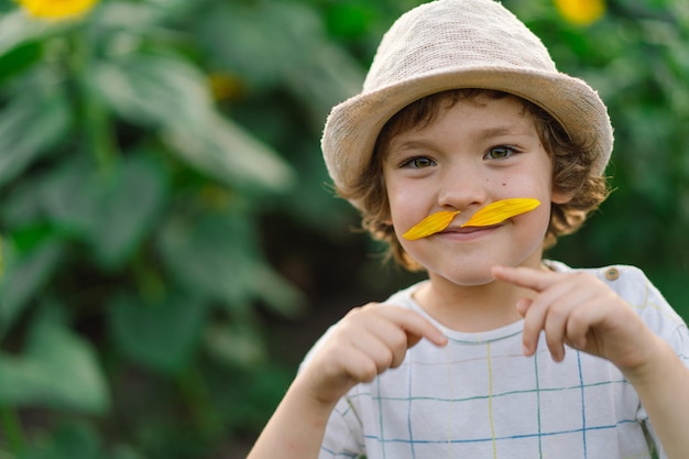 Un ragazzino felice che cammina in un campo di girasoli e si fa i baffi con i petali di girasole