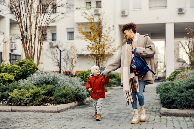 Un ragazzino felice che si tiene per mano con la sua babysitter e va all'asilo