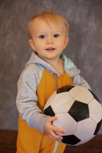 Un ragazzino felice con una tuta gialla e grigia giace accanto a un pallone da calcio