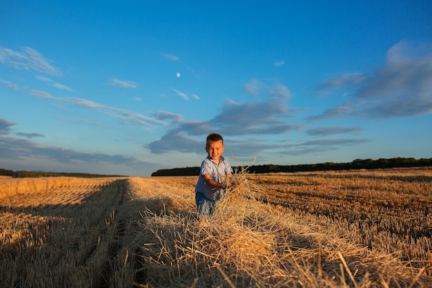 Un ragazzino gioca in un campo di grano sullo sfondo di un cielo blu e di una luna