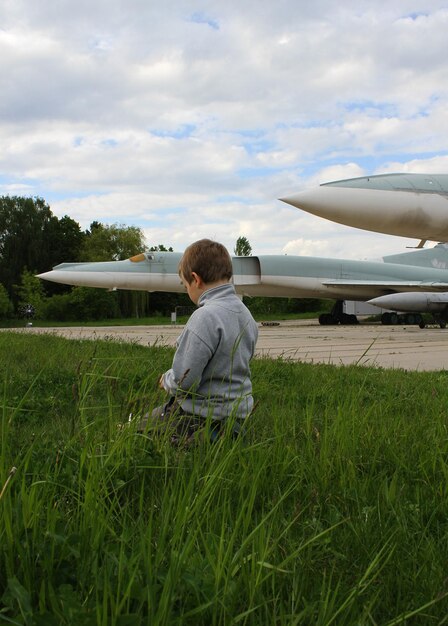 Un ragazzino gioca nell'erba vicino a un terreno di cemento con razzi vicino a un aereo militare