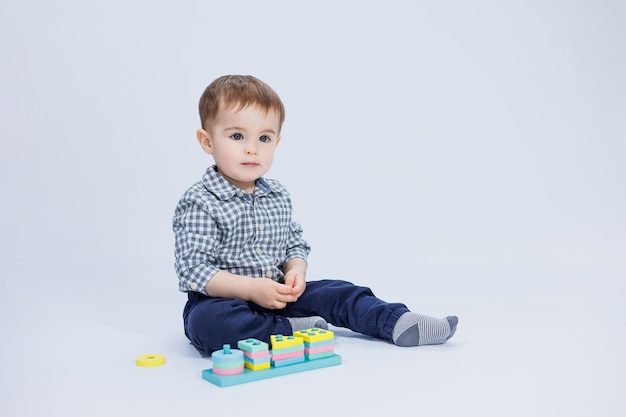 Un ragazzino in una camicia sta costruendo un giocattolo di legno colorato su uno sfondo bianco Il concetto di giochi di sviluppo per bambini per giocattoli per bambini Copia spazio