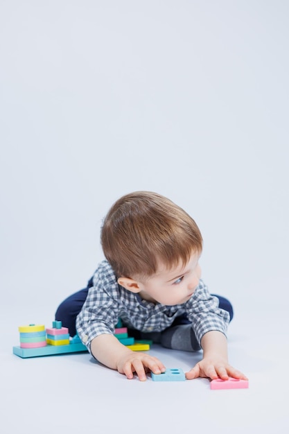 Un ragazzino in una camicia sta costruendo un giocattolo di legno colorato su uno sfondo bianco Il concetto di giochi di sviluppo per bambini per giocattoli per bambini Copia spazio