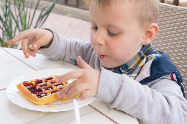 Un ragazzino mangia cialde belghe da dessert con marmellata in un caffè
