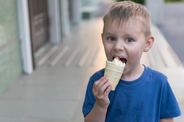 Un ragazzino mangia il gelato Il bambino si lascia trasportare mangiando un gelato al limone e cioccolato in una tazza di cialda Delicatezza per bambini