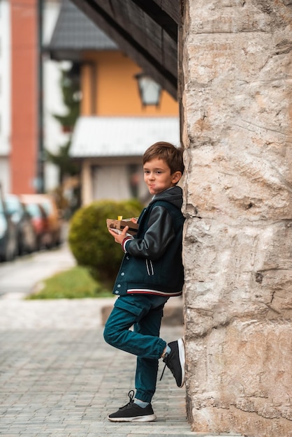 Un ragazzino moderno posa in città mentre mangia poffertjes freschi e gustosi Messa a fuoco selettiva