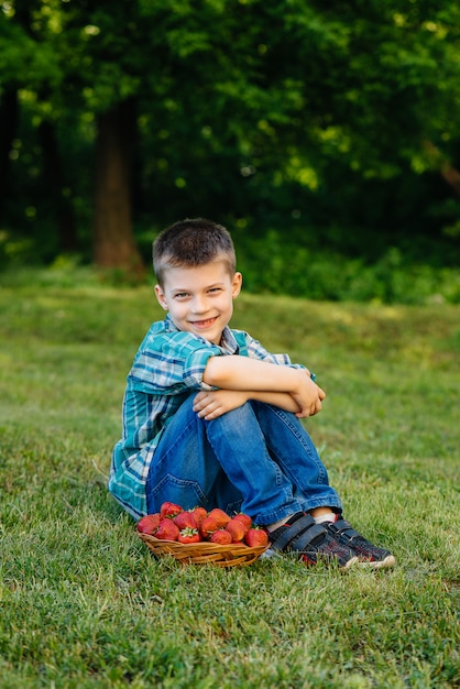 Un ragazzino nel parco con un grande cesto di fragole.