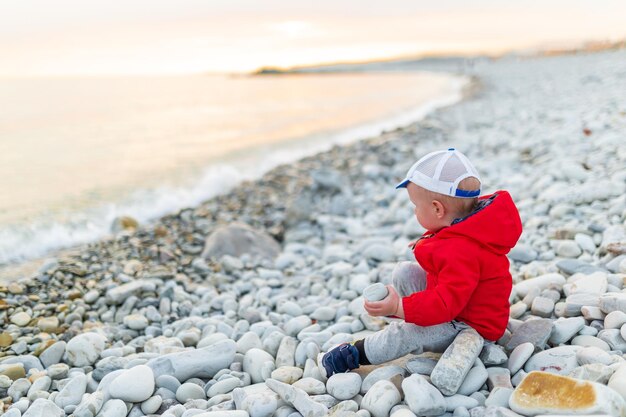 Un ragazzino si siede su una spiaggia sassosa e guarda il mare blu Bambino su una spiaggia che guarda il mare