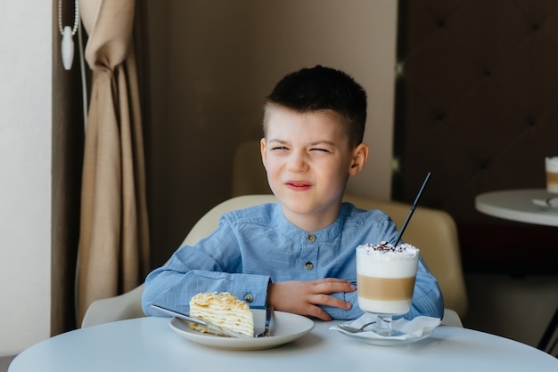 Un ragazzino sveglio è seduto in un caffè e guarda una torta e un primo piano di cacao. Dieta e corretta alimentazione.