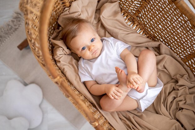 un ragazzino un bambino biondo con gli occhi blu in un vestito bianco giace sulla schiena in una culla di vimini a casa nella nursery il sogno di un bambino di un bambino