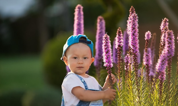 Un ragazzino vestito in modo vivace sta giocando con grandi fiori viola nel cortile sul retro