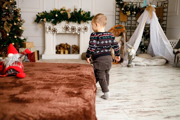 Un ragazzo a casa corre all'albero di Natale per trovare i regali di Babbo Natale Vestiti invernali caldi