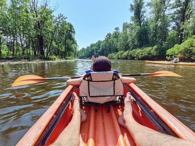 Un ragazzo adolescente nuota con un remo in un kayak sul fiume sullo sfondo degli alberi