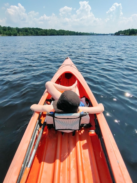 Un ragazzo adolescente sta nuotando in un kayak sul fiume in un giubbotto di salvataggio e riposando vista posteriore