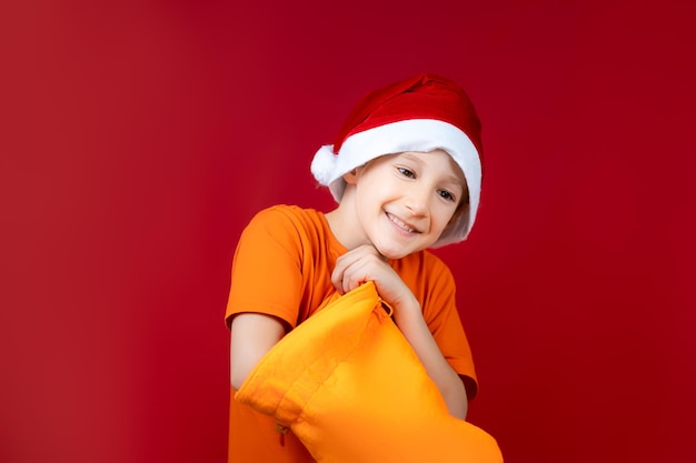 Un ragazzo allegro con un cappello da Babbo Natale infila la mano in una borsa gialla di Natale e sorride