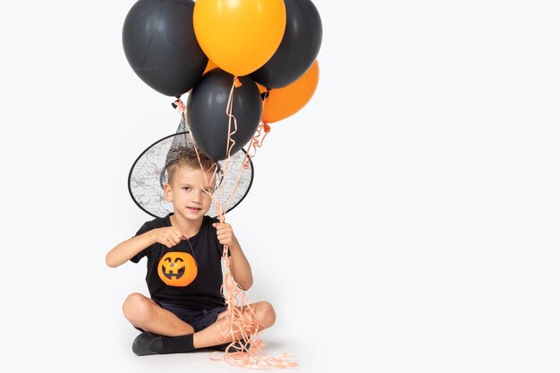 Un ragazzo allegro e felice con un cappello da mago che tiene un secchio a forma di zucca e palloncini neri e arancioni