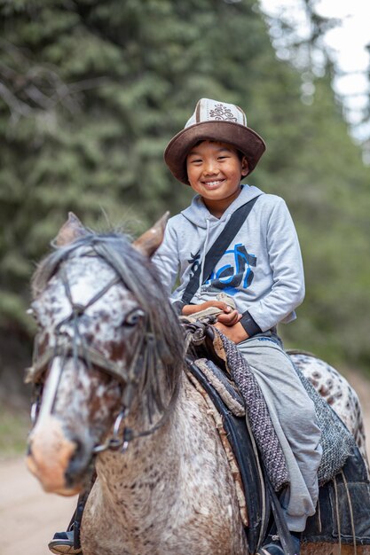 Un ragazzo asiatico carino e sorridente con un cappello nazionale che cavalca un cavallo va in montagna e incontra i turisti