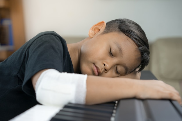 Un ragazzo asiatico con le mani ferite sta dormendo sul pianoforte.