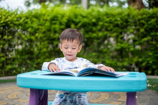 Un ragazzo asiatico di 1 anno sta aprendo intensamente un libro di lettura nel suo parco Immagine dello spazio di copia