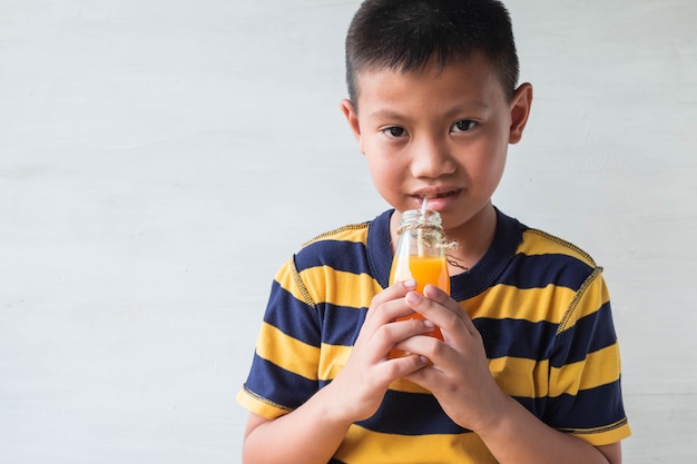 Un ragazzo asiatico sta bevendo una bottiglia di succo d'arancia.