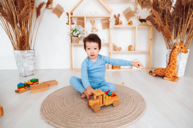 Un ragazzo asiatico sta giocando con una piccola macchina di legno Un ragazzino sta giocando con i cubi sorridendo il bambino è seduto per terra e sta giocando con una macchina da scrivere