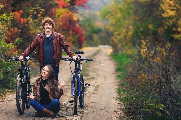 Un ragazzo baffuto dai capelli ricci e una ragazza dai capelli minerali in autunno stanno con le biciclette sulla strada e mostrano emozioni allegre